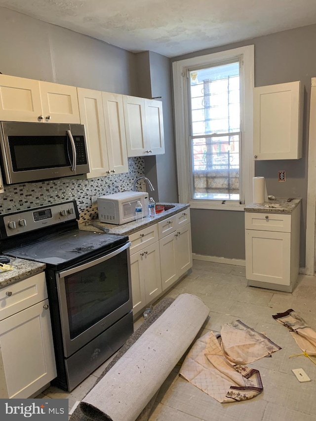 kitchen with decorative backsplash, light stone counters, white cabinetry, and appliances with stainless steel finishes