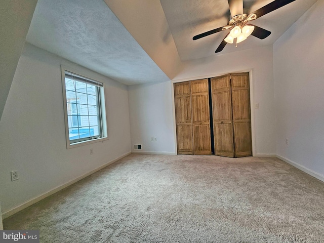 unfurnished bedroom featuring ceiling fan, light colored carpet, vaulted ceiling, a textured ceiling, and a closet