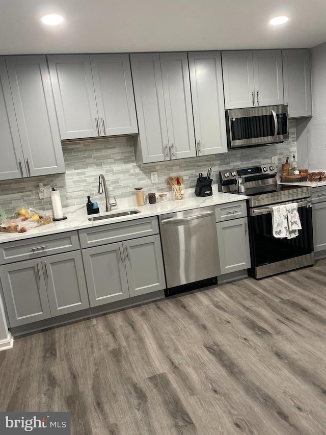 kitchen featuring gray cabinetry, sink, stainless steel appliances, tasteful backsplash, and wood-type flooring