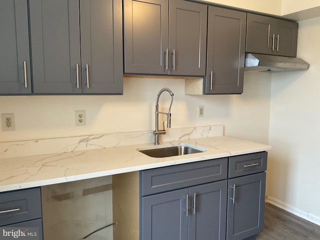 kitchen with dark wood-type flooring, gray cabinets, light stone countertops, and sink