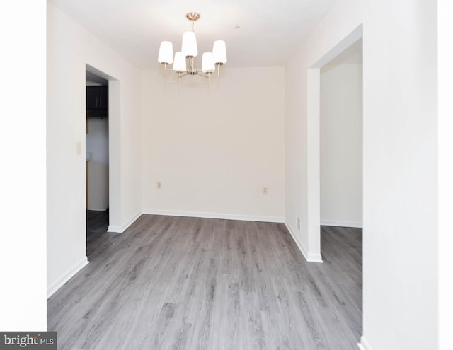 spare room with a notable chandelier and light wood-type flooring