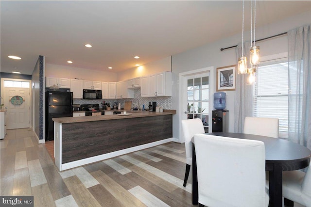 kitchen featuring white cabinets, decorative light fixtures, black appliances, and light hardwood / wood-style flooring