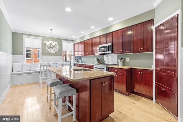 kitchen with sink, stainless steel appliances, decorative light fixtures, a kitchen island with sink, and ornamental molding