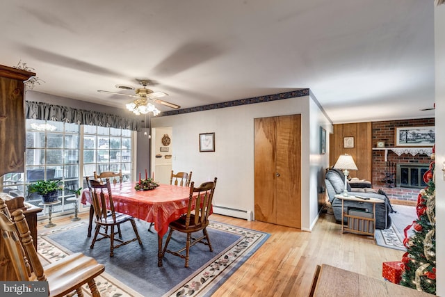 dining room featuring baseboard heating, a brick fireplace, ceiling fan, and light wood-type flooring