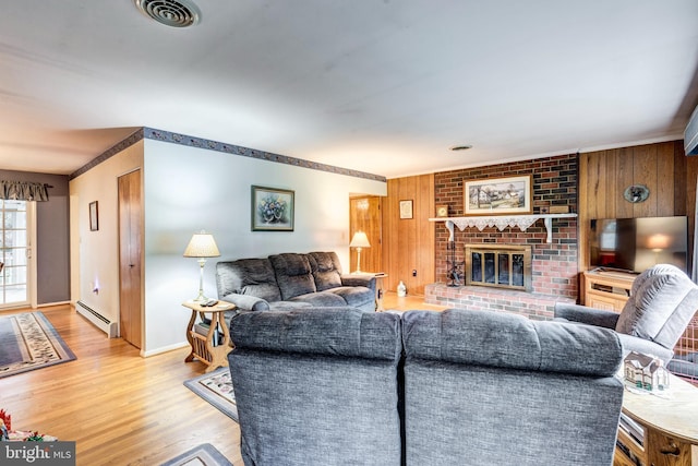 living room with wood walls, a brick fireplace, ornamental molding, light wood-type flooring, and baseboard heating