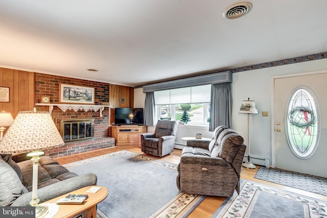 living room featuring wood walls, wood-type flooring, a baseboard radiator, and a brick fireplace