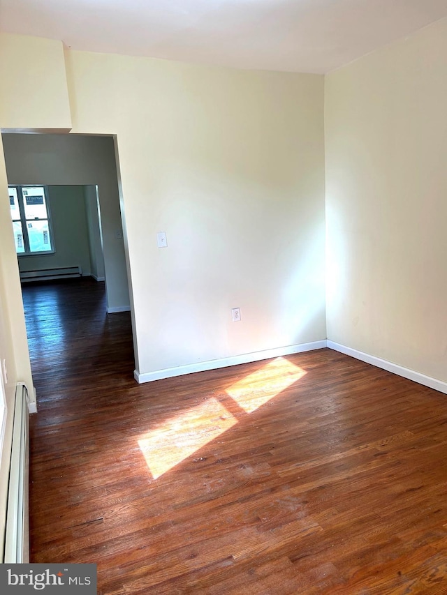 empty room with baseboard heating and dark hardwood / wood-style floors