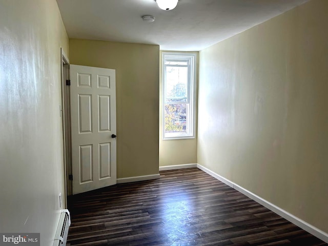 unfurnished room featuring dark wood-type flooring and a baseboard heating unit