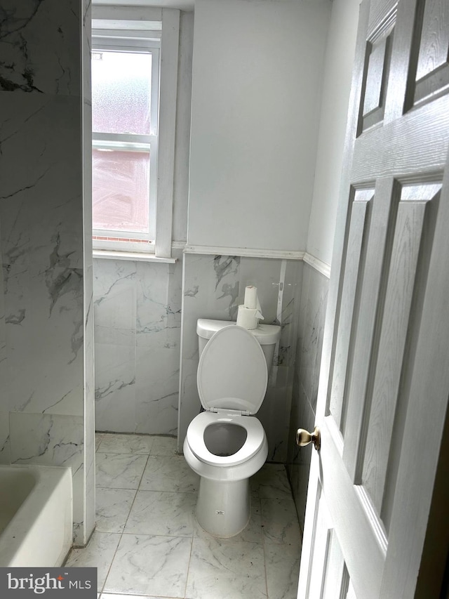 bathroom featuring a bath, toilet, and tile walls