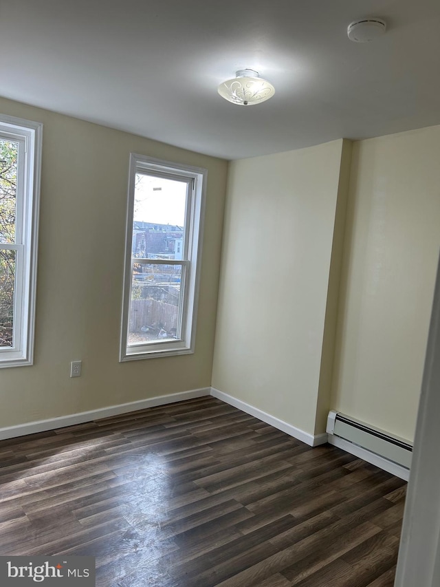 spare room featuring a healthy amount of sunlight, dark hardwood / wood-style flooring, and a baseboard radiator