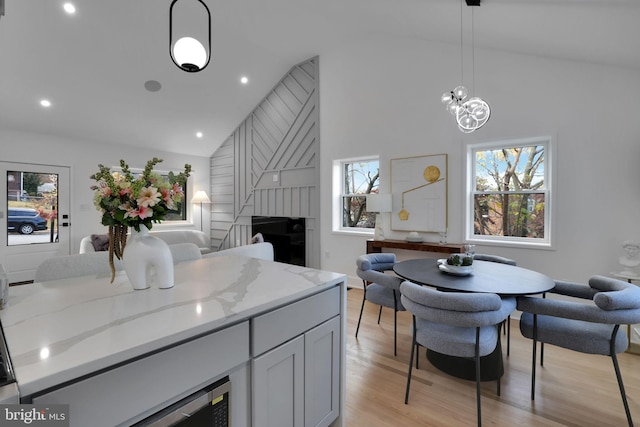 kitchen with pendant lighting, high vaulted ceiling, light wood-type flooring, light stone countertops, and a notable chandelier