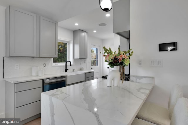 kitchen with gray cabinetry, sink, light stone counters, stainless steel dishwasher, and backsplash