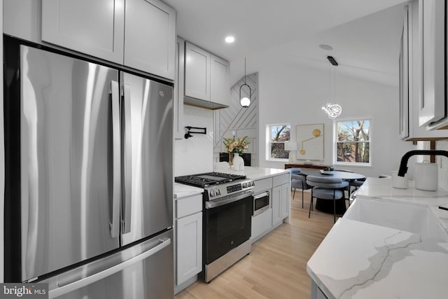 kitchen with pendant lighting, lofted ceiling, white cabinets, light wood-type flooring, and appliances with stainless steel finishes