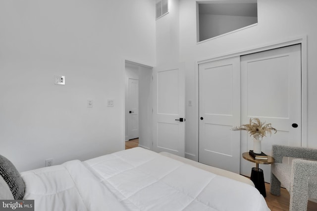 bedroom with hardwood / wood-style floors, high vaulted ceiling, and a closet