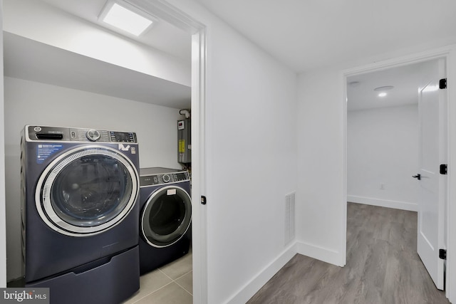 clothes washing area with washer and dryer, light wood-type flooring, and gas water heater