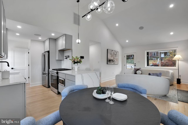 dining area with light wood-type flooring, sink, and high vaulted ceiling