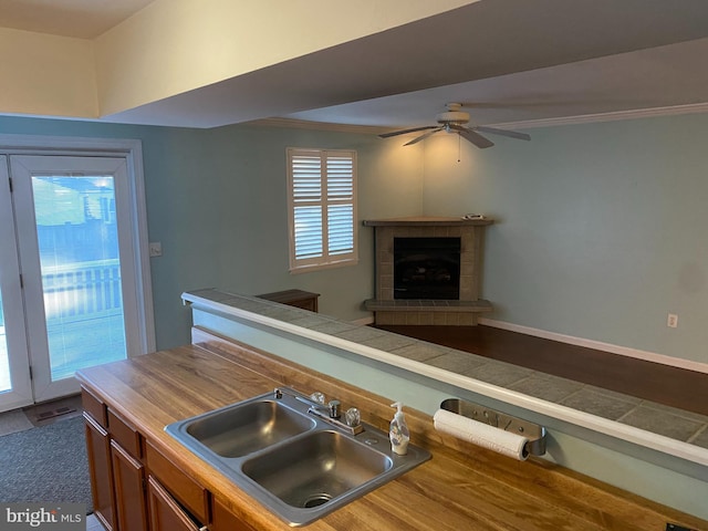 kitchen featuring ornamental molding, ceiling fan, sink, a tile fireplace, and tile counters