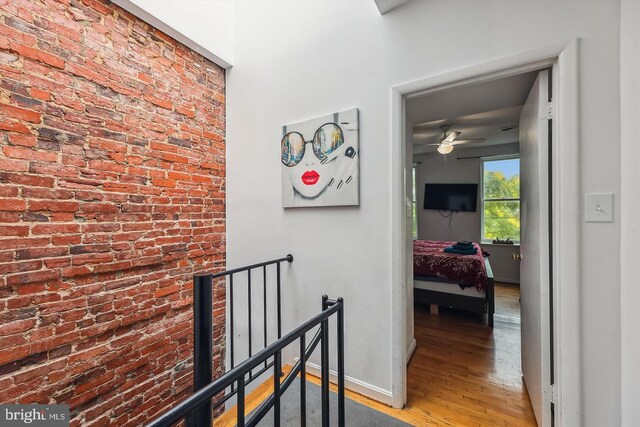 corridor with wood-type flooring and brick wall