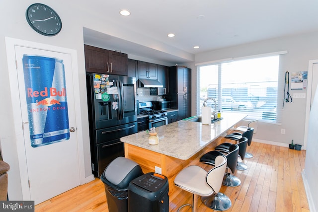 kitchen with sink, gas stove, black fridge with ice dispenser, and an island with sink