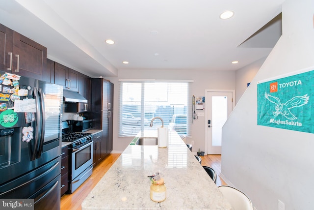 kitchen featuring light stone countertops, sink, light hardwood / wood-style flooring, a center island with sink, and appliances with stainless steel finishes