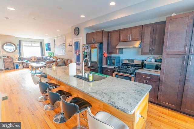 kitchen with a kitchen breakfast bar, light stone counters, appliances with stainless steel finishes, and light hardwood / wood-style flooring