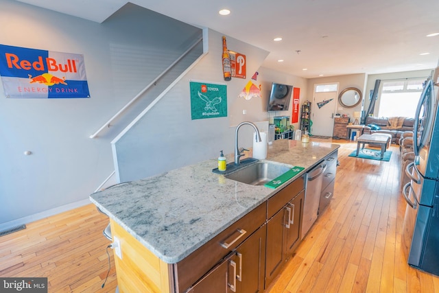 kitchen featuring light stone countertops, sink, light hardwood / wood-style floors, fridge, and a center island with sink