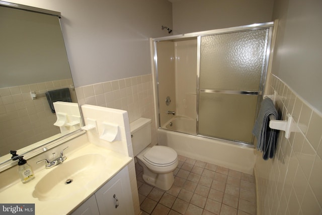 full bathroom featuring bath / shower combo with glass door, toilet, vanity, and tile walls