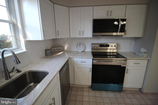 kitchen featuring white cabinetry, stainless steel appliances, tasteful backsplash, sink, and light tile patterned floors