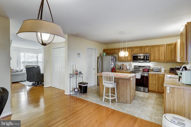 kitchen with a center island, light hardwood / wood-style flooring, decorative light fixtures, and appliances with stainless steel finishes