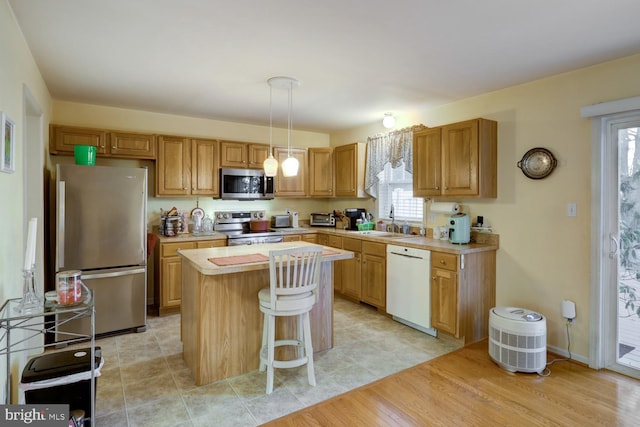 kitchen with sink, hanging light fixtures, stainless steel appliances, light hardwood / wood-style flooring, and a kitchen island