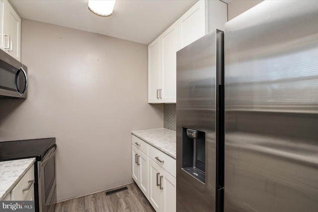 kitchen featuring decorative backsplash, appliances with stainless steel finishes, light wood-type flooring, light stone counters, and white cabinets