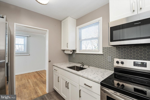 kitchen with sink, light stone counters, appliances with stainless steel finishes, white cabinets, and hardwood / wood-style flooring