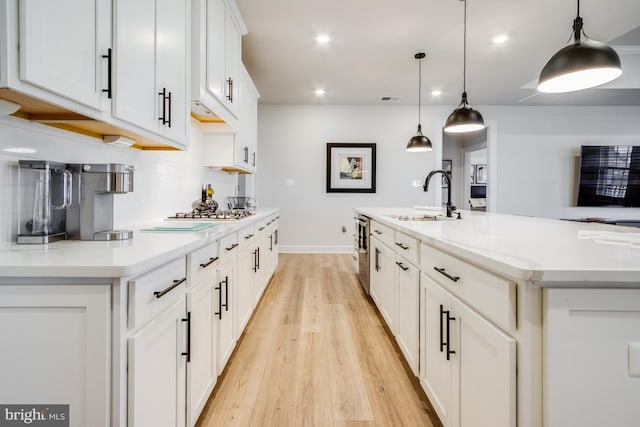 kitchen with a spacious island, sink, pendant lighting, white cabinets, and light hardwood / wood-style floors