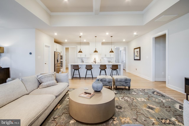 living room with sink, light wood-type flooring, and ornamental molding