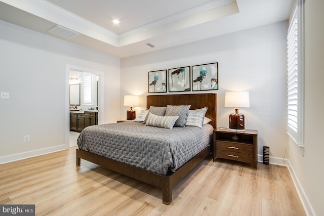 bedroom with light wood-type flooring, ensuite bathroom, a tray ceiling, and ornamental molding