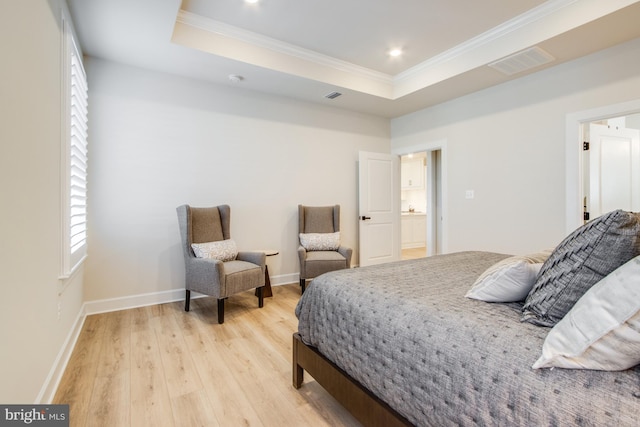 bedroom with ensuite bathroom, a raised ceiling, light wood-type flooring, and ornamental molding