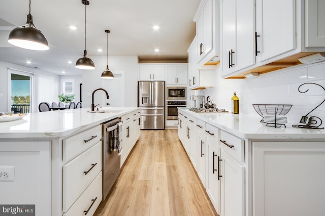 kitchen featuring white cabinets, decorative light fixtures, stainless steel appliances, and a kitchen island with sink