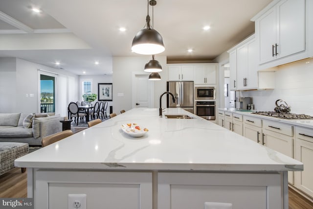 kitchen with light stone countertops, a large island, sink, pendant lighting, and appliances with stainless steel finishes