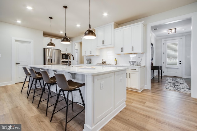 kitchen featuring stainless steel appliances, white cabinetry, a center island with sink, and light hardwood / wood-style floors