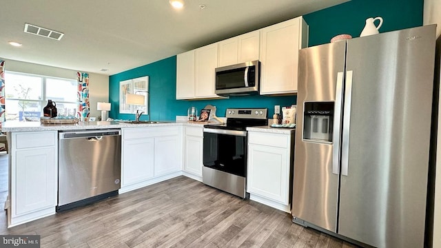 kitchen with white cabinets, appliances with stainless steel finishes, light hardwood / wood-style floors, and sink