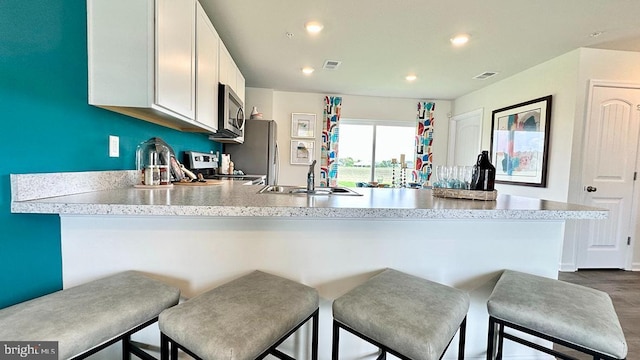 kitchen with white cabinetry, sink, stainless steel appliances, dark hardwood / wood-style floors, and kitchen peninsula