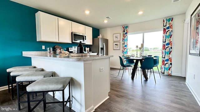 kitchen featuring kitchen peninsula, appliances with stainless steel finishes, dark hardwood / wood-style flooring, a kitchen breakfast bar, and white cabinetry