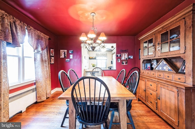 dining room with radiator, light hardwood / wood-style flooring, and a notable chandelier