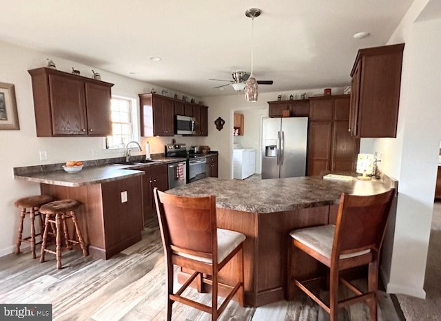 kitchen with a breakfast bar, light wood-type flooring, separate washer and dryer, kitchen peninsula, and stainless steel appliances