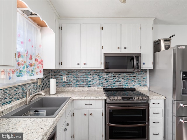 kitchen with decorative backsplash, appliances with stainless steel finishes, white cabinetry, a sink, and light stone countertops