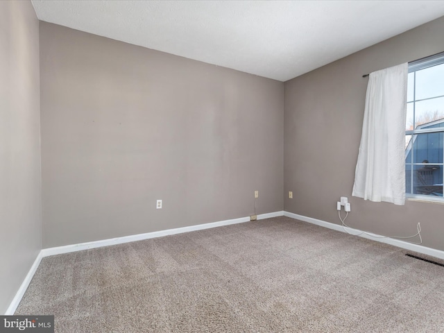 spare room with carpet flooring, visible vents, and baseboards