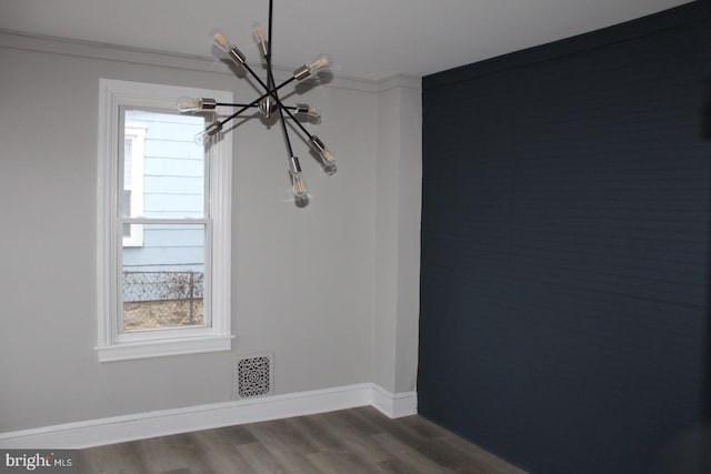 empty room featuring hardwood / wood-style floors, ornamental molding, and a notable chandelier