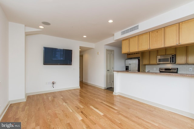 kitchen with light wood-type flooring, stainless steel appliances, and tasteful backsplash