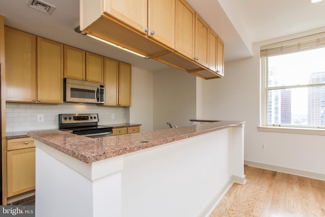 kitchen with light brown cabinets, decorative backsplash, a kitchen island, light hardwood / wood-style floors, and stainless steel appliances