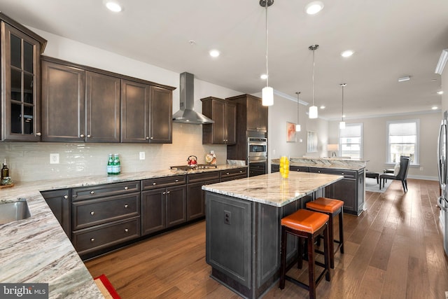 kitchen with hanging light fixtures, dark brown cabinets, dark hardwood / wood-style floors, and wall chimney range hood